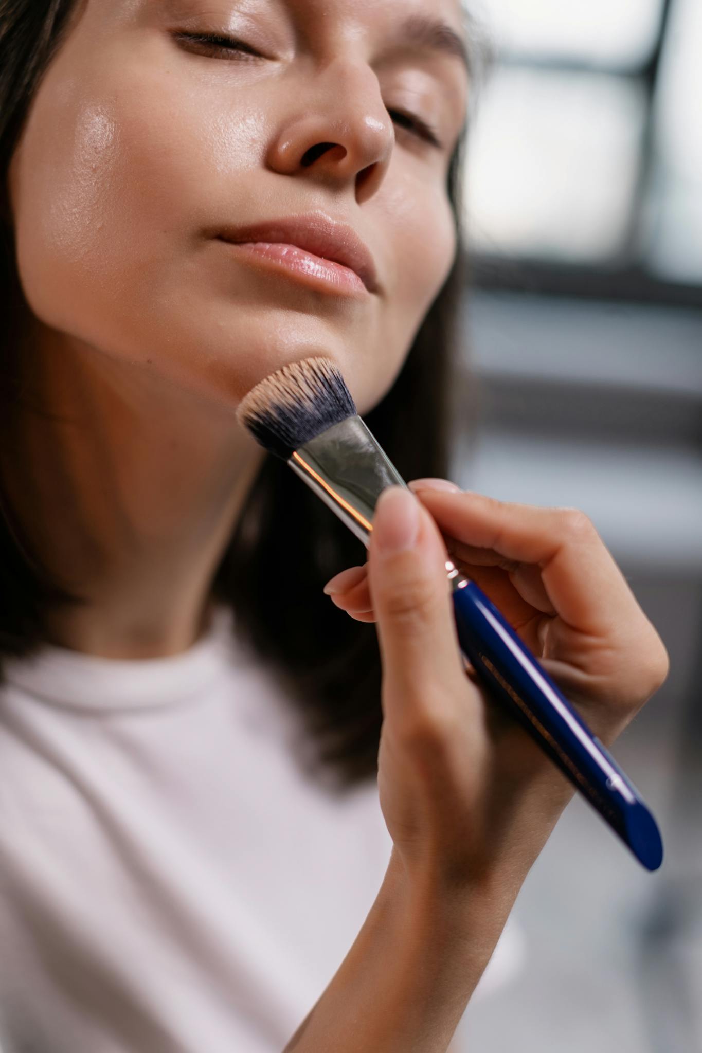 Close-up of a woman using a makeup brush to apply foundation indoors.