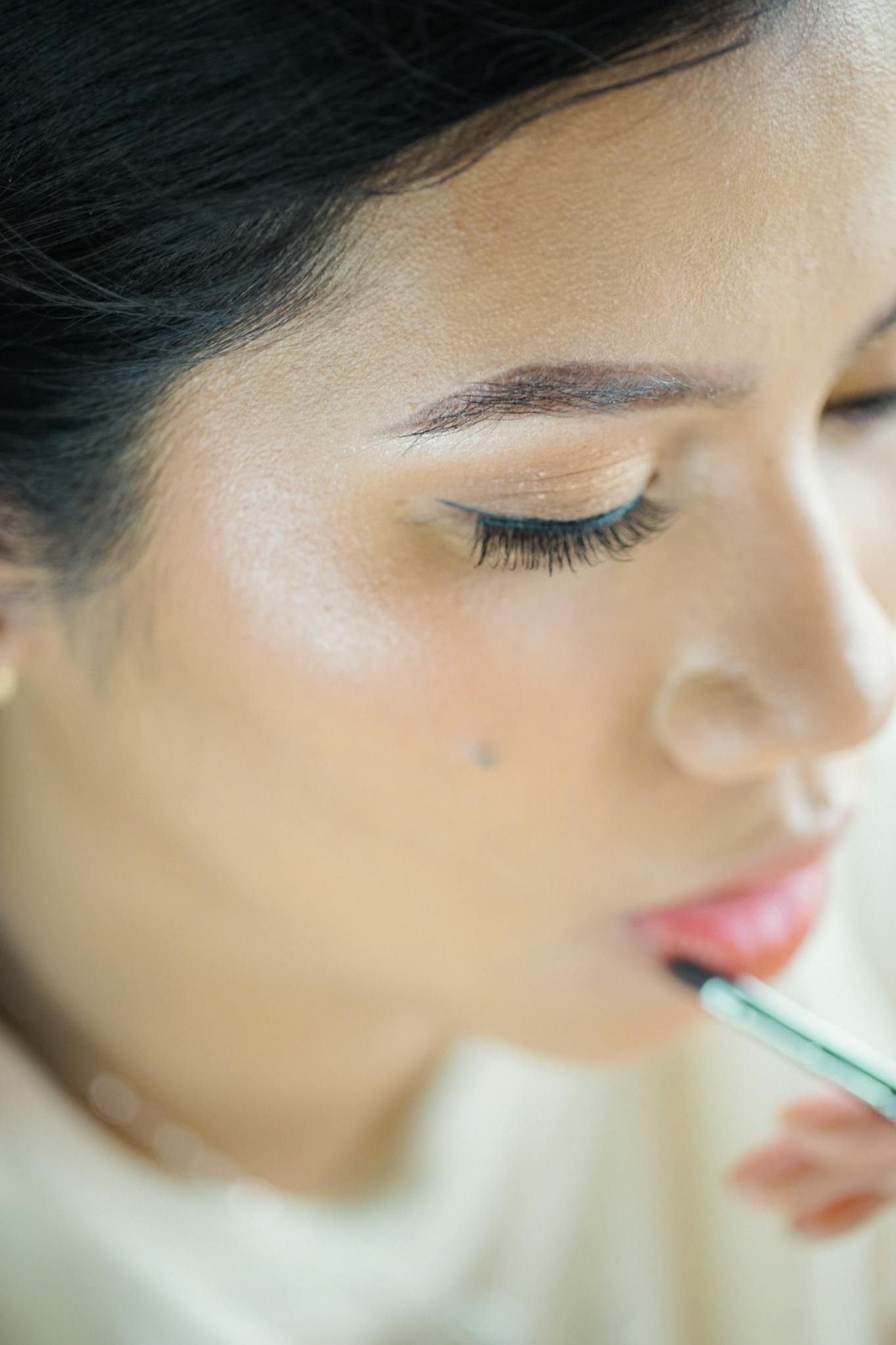 Detailed portrait of a woman applying makeup, highlighting beauty and precision.